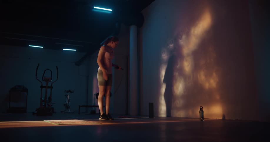 A woman exercises with a jump rope before resting against a wall and drinking from a water bottle