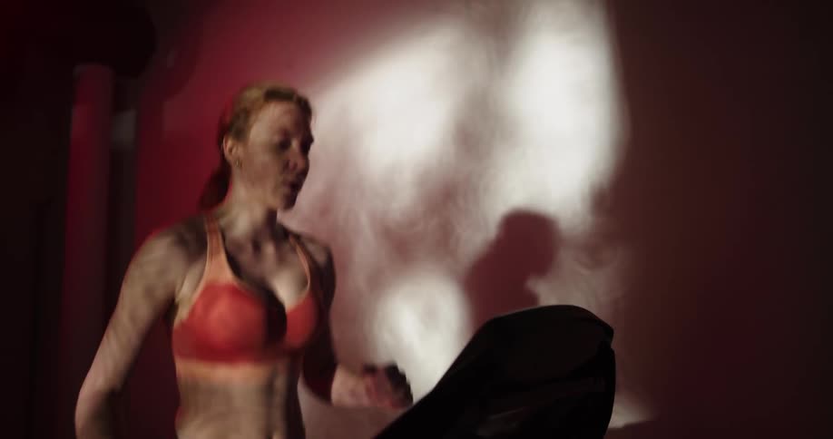 Woman casts shadow on wall as she runs on treadmill in dim gym