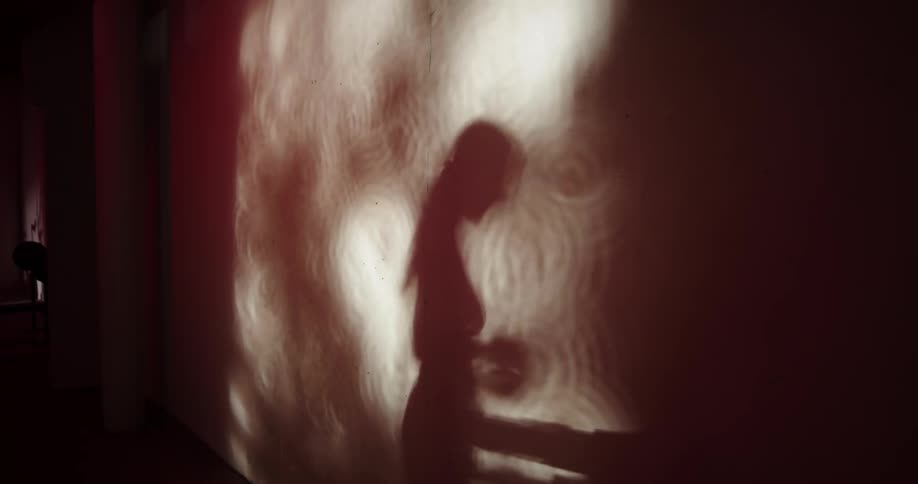 A shadow of a woman running on a treadmill projected onto a wall