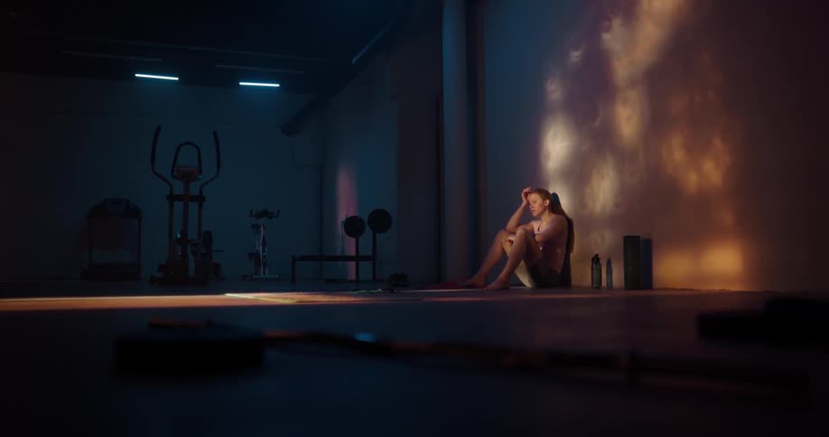 Woman with ponytail shirt and shorts sits against the wall using smartphone and toss it away in anger