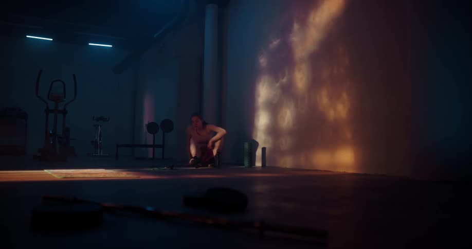 Woman with ponytail shirt and shorts sits on yoga mat at the gym