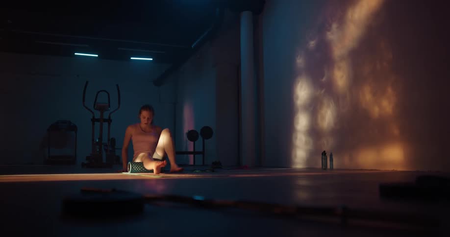 Woman exercises with rolling tube on floor in dimly lit gym