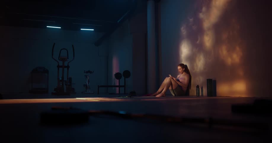 Woman with ponytail shirt and shorts sits and uses mobile phone at the gym