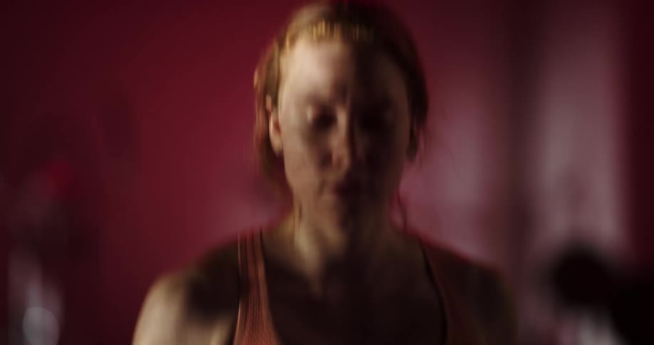 A young woman wearing a red sports bra is running indoors on an unseen treadmill
