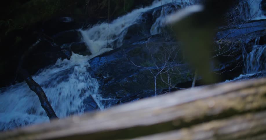 Man with jeans and green boots walks on tree trunk over stream