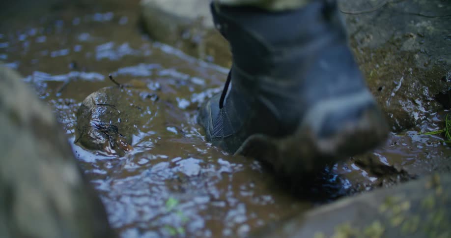 A person in boots stepping in a muddy puddle while walking outdoors