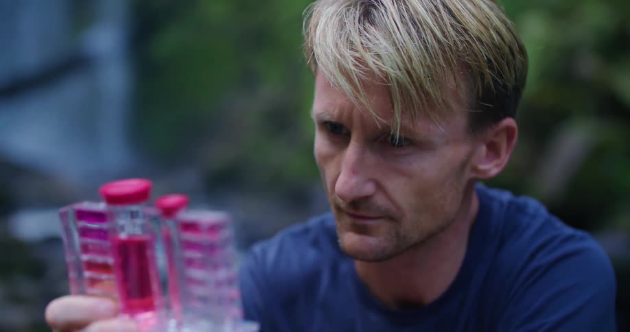 A man testing water samples next to a river in nature