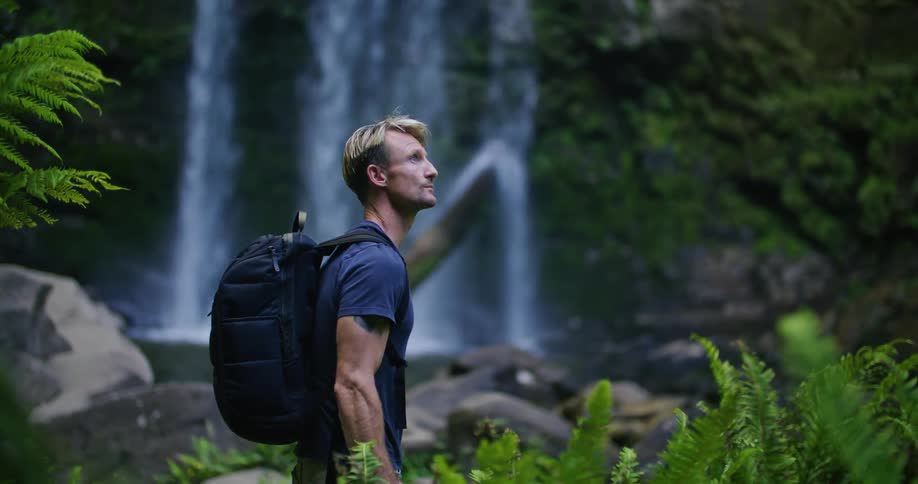 A man is standing by the waterfall