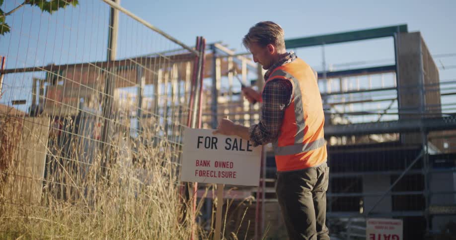 A construction worker hammering a for sale sign into the ground