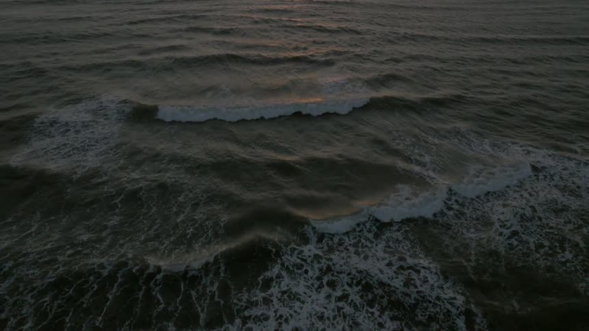 Ocean waves rolling into the beach as the sun sets