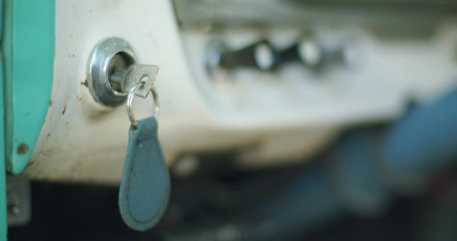 A key is in the ignition of an old automobile as the keychain gently rocks back and forth
