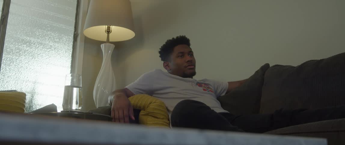 A man lounging on a couch while watching something and adjusting himself in position