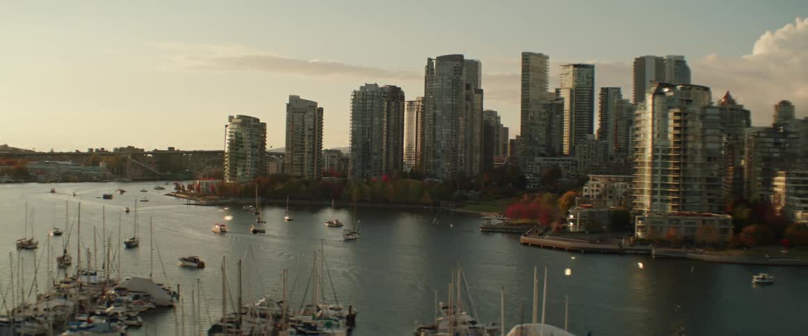Boats sail through water between marina and Vancouver's downtown skyscrapers during the fall