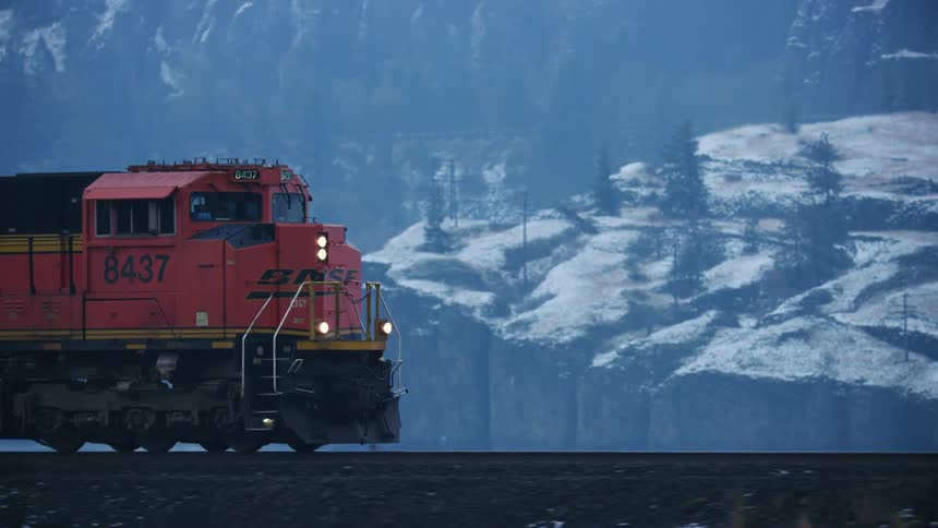 Freight train runs along railway truck with snowy mountains in the background