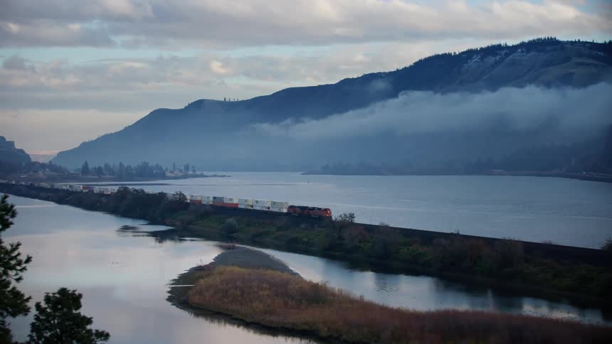 A freight train pulling cargo riverside on a foggy and chilly morning in the Pacific Northwest