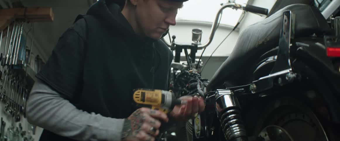 A mechanic is holding a drill and working on a motorcycle