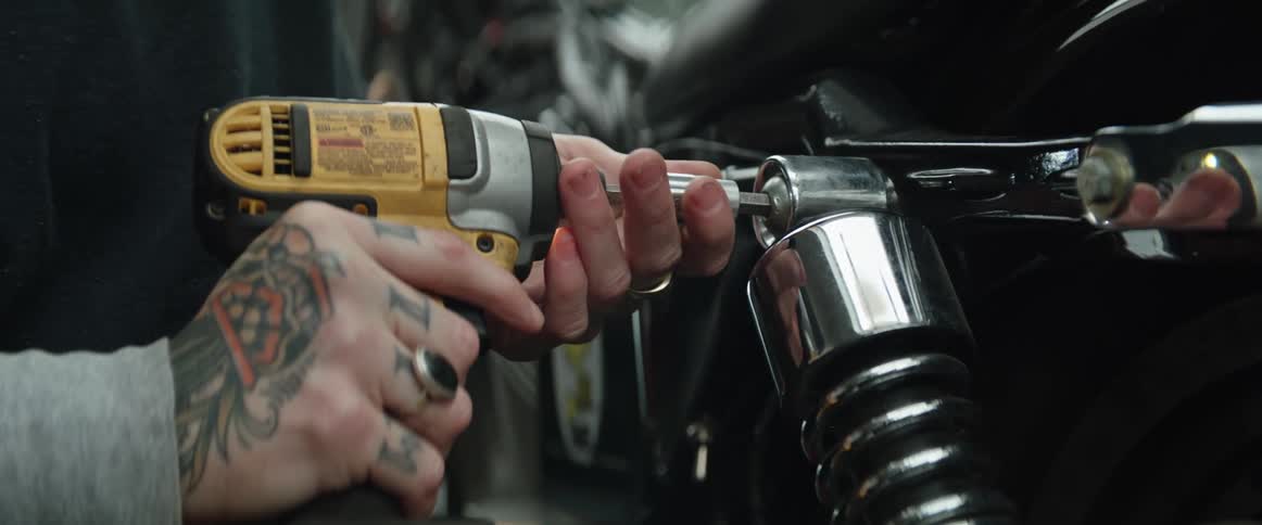 A mechanic is holding a drill and working on a motorcycle