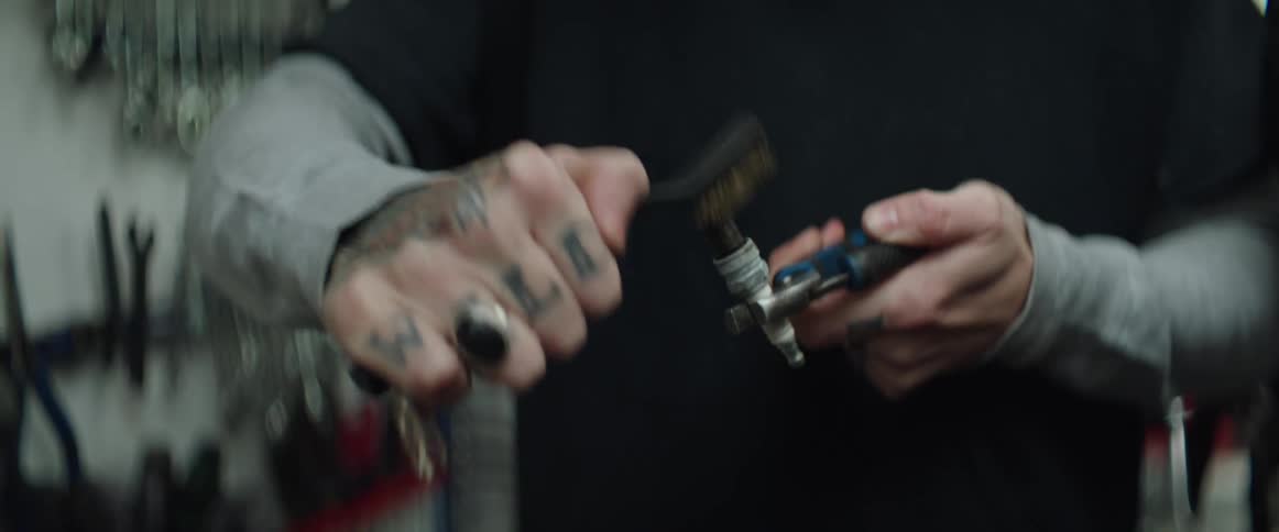 A mechanic is holding a spark plug with pliers and cleaning it with a wire brush