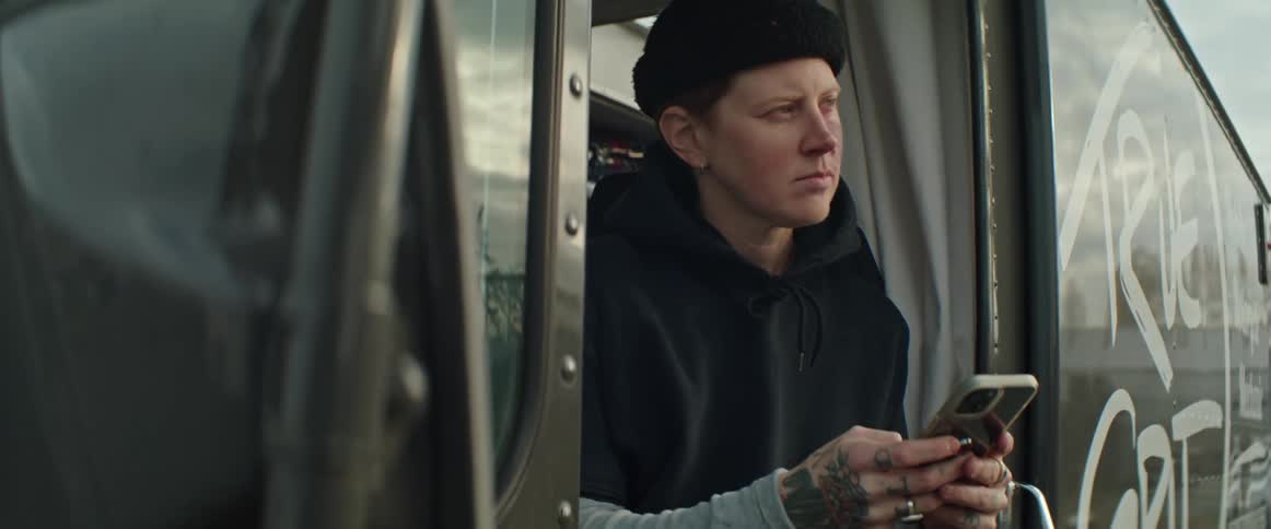 A woman is sitting outside in the doorway of a vehicle holding her phone and looking up
