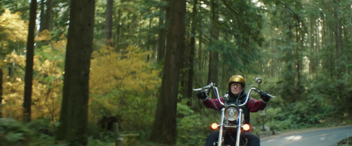 A woman is riding a motorcycle on a winding road through the woods