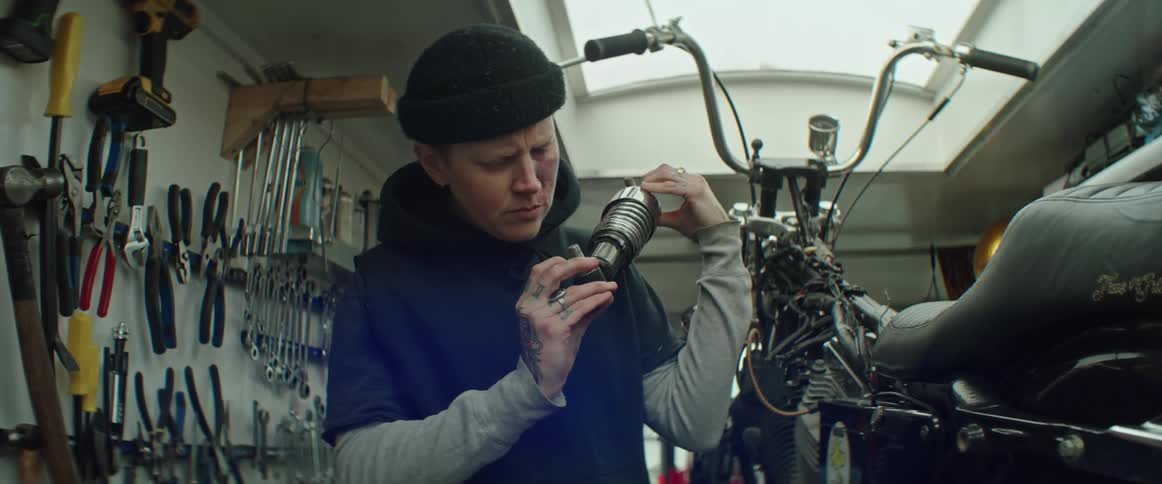 A person holding a bike part next to a motorcycle looking at it closely