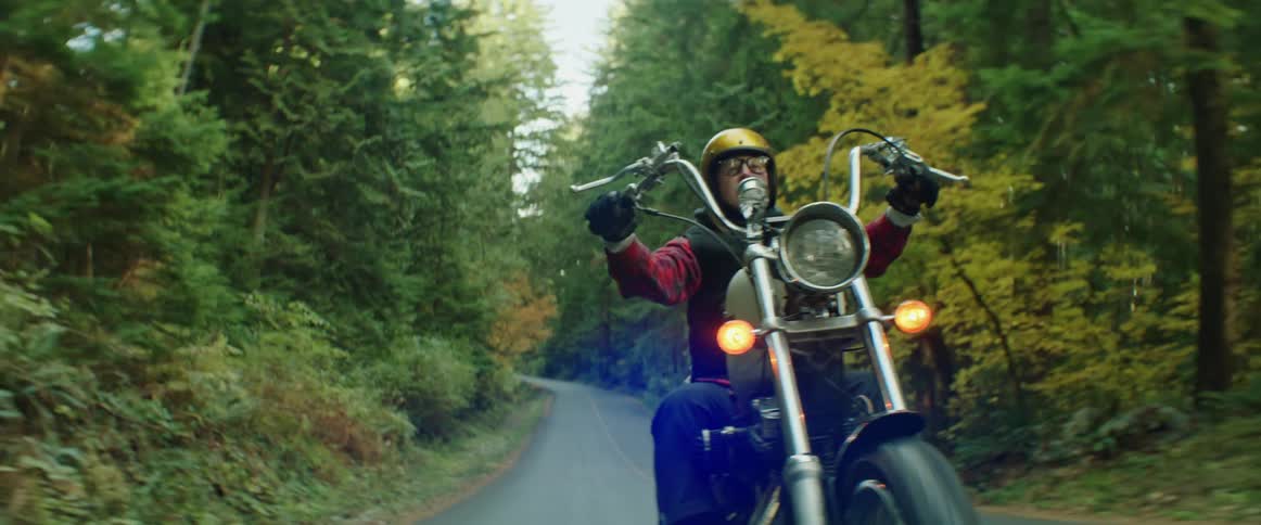 A person riding a motorcycle wearing a yellow helmet driving down a road surrounded by trees