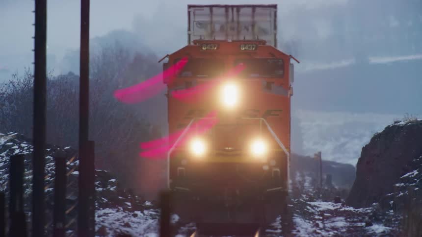 A freight train locomotive with headlights on among rocks during the winter