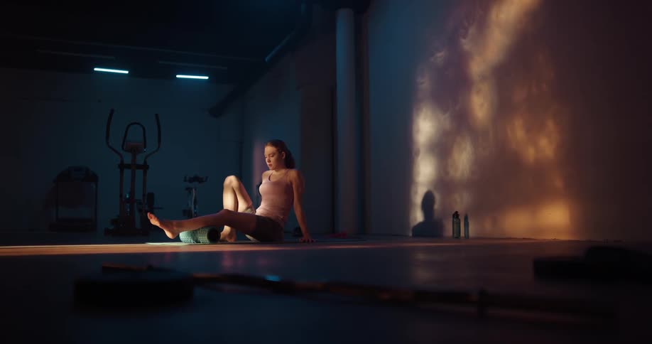 Woman with ponytail pink sports shirt and shorts uses yoga roller in a gym