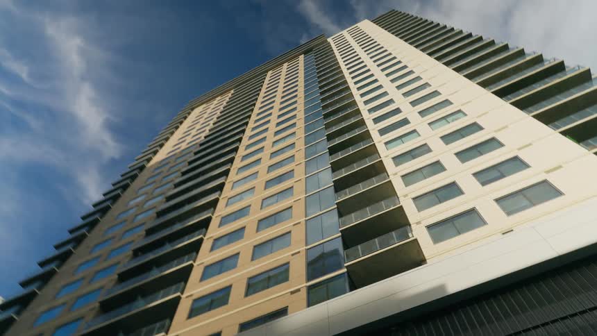 Wispy clouds float over a tall apartment building in a city
