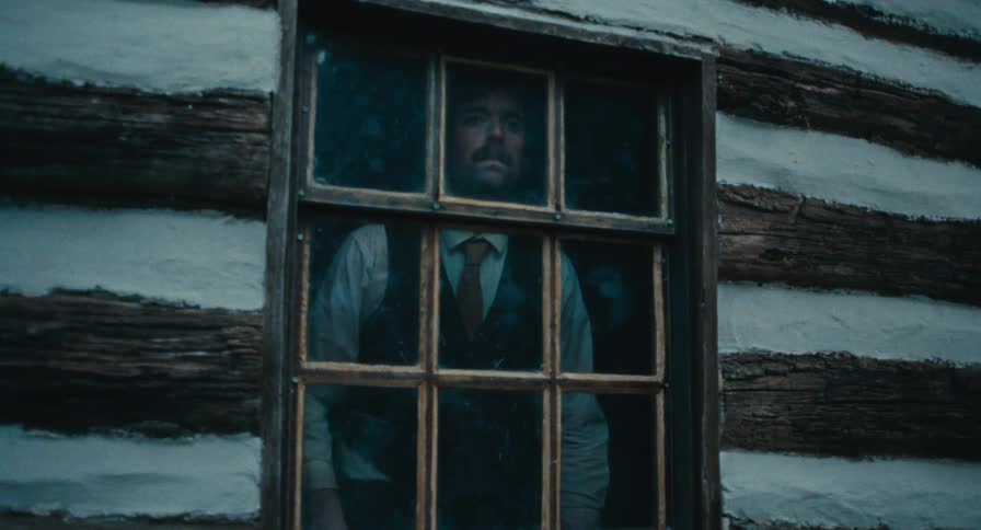 A man nervously looks out the window of a cabin