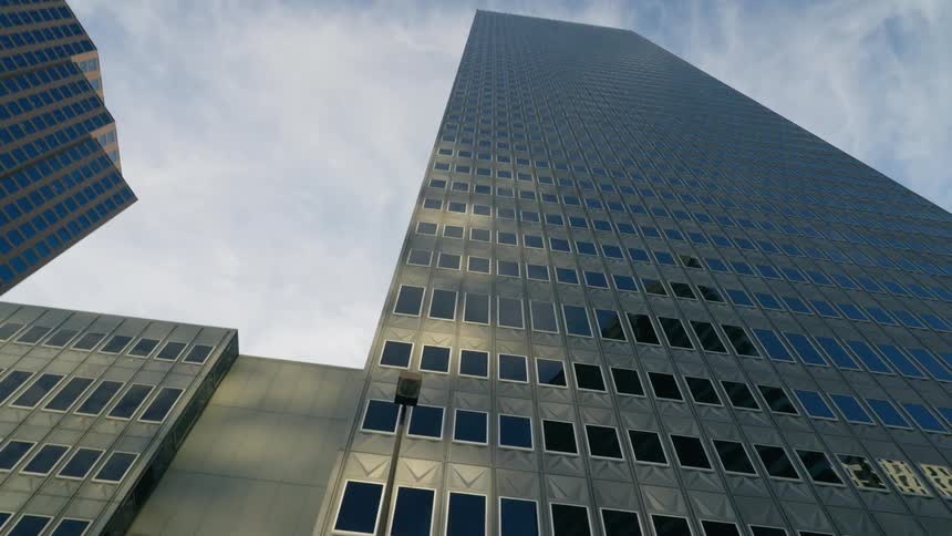 Windows of skyscraper reflect other downtown buildings under a cloudy sky