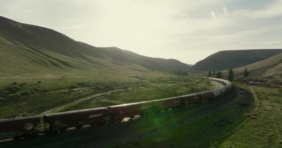Sunlight glints along freight cars moving through green rolling hills
