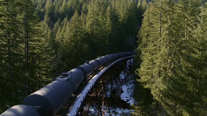Tank cars travel through the woods and cross a bridge over a mountain river