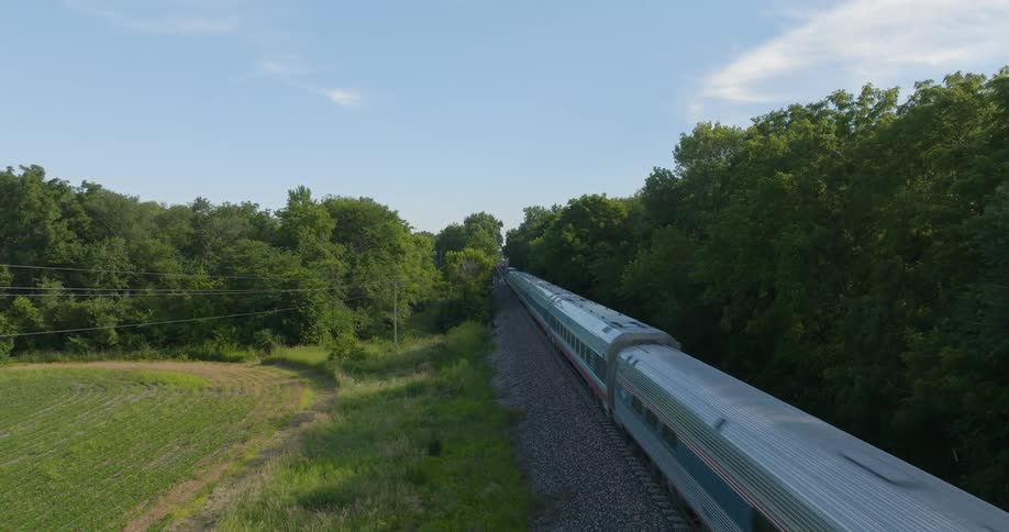 A passenger train speeds by rural farmland and countryside on a bright sunny day