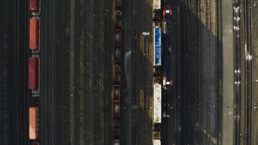 A slow freight train casts long shadows along one of many parallel tracks in a switching yard