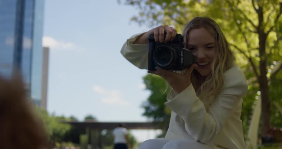 Blonde woman taking video of dog in park near downtown smiles at the animal