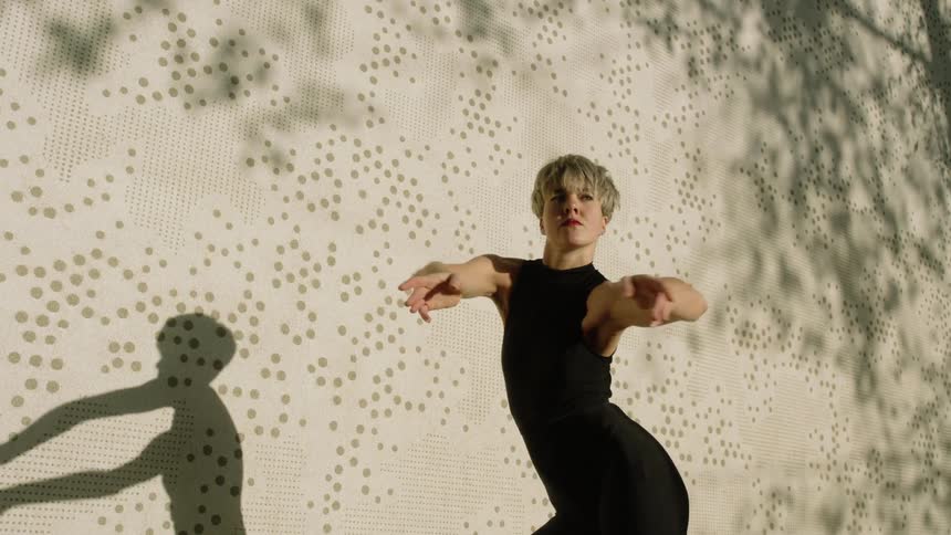 Female dancer casts shadow on exterior wall as she dances