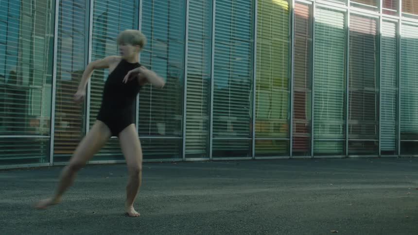 A young woman dances in front of large windows covered with blinds
