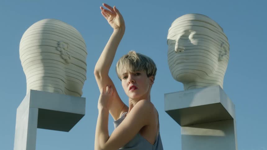 A woman dancing with her arms between two head sculptures