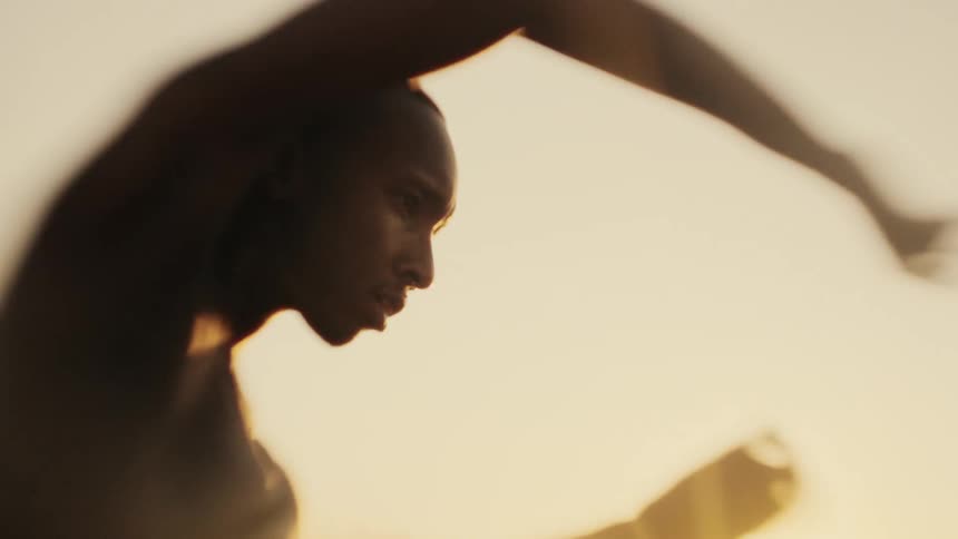 The sun shines brightly upon a man standing outside dancing with his arms in the air