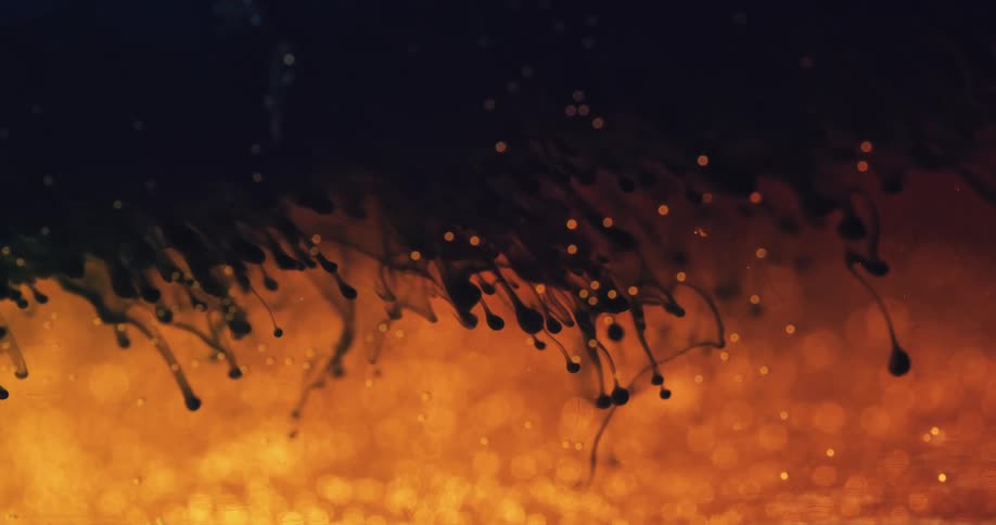 Small orange spheres rise from a moving orange substance in the darkness