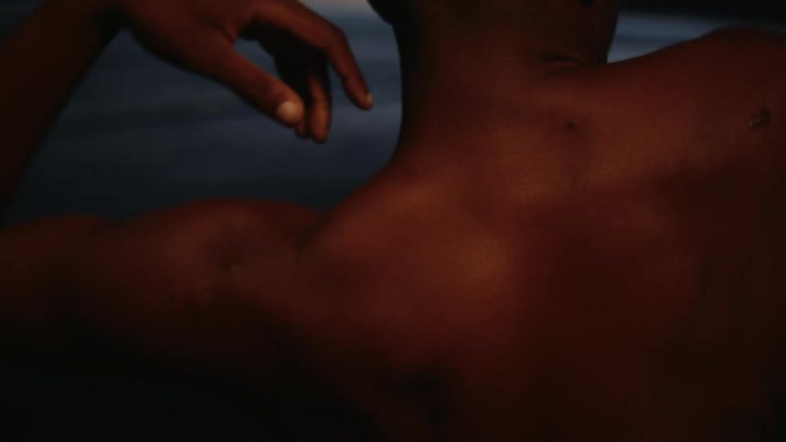 A bare shouldered man dancing on a beach at sunset