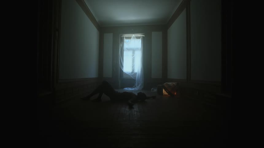 Silhouette of a man laying on the floor of a dark hallway in front of a window