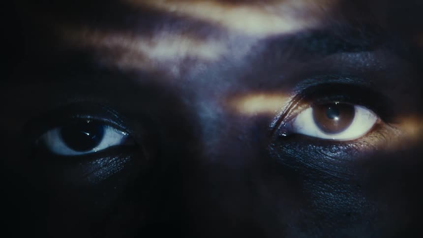 Close up of the eyes of a man looking at the camera under shifting slits of light