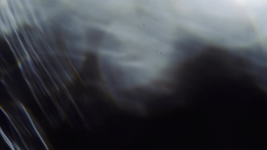 Blurry out of focus footage of the silhouette of shapes behind a waving water like screen