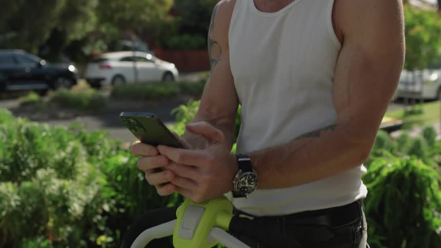 A man mowing and stopping to check his cellphone smiling slightly