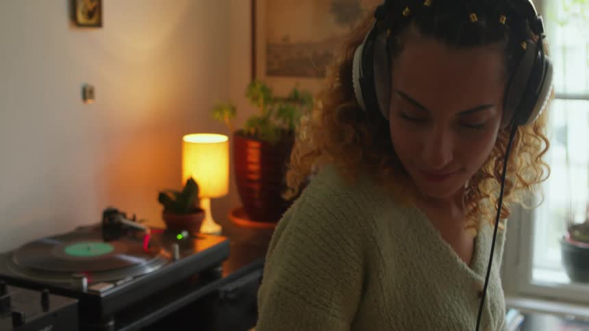 A woman wears headphones while dancing around her living room