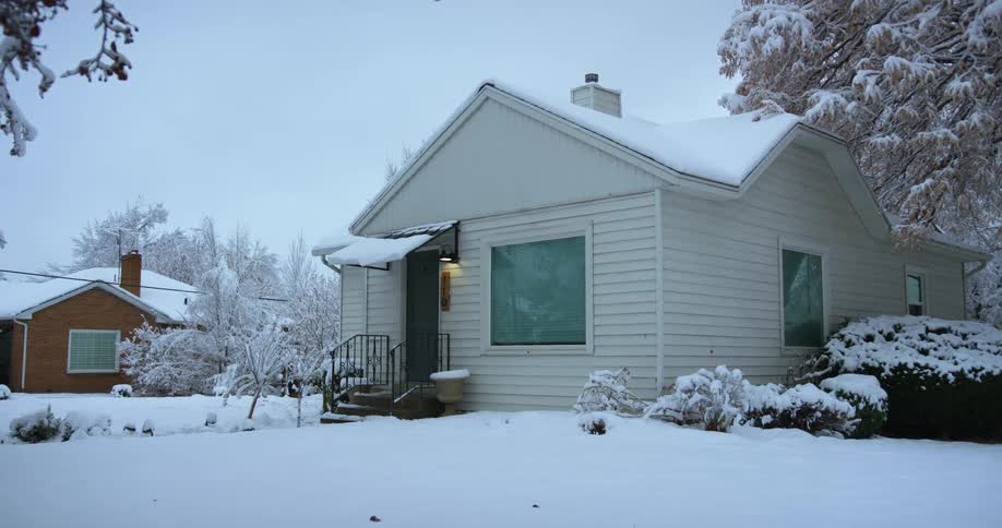 The porch light on a house is on in a snow covered neighborhood on a winter day