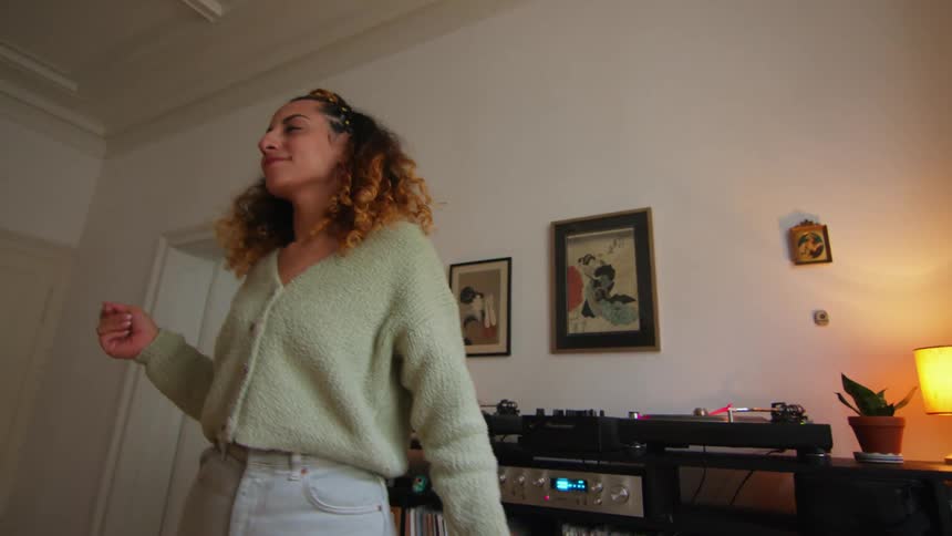 A woman dances around her living room while listening to an vinyl album