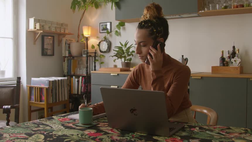 A woman taking notes while making a phonecall at home